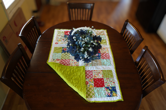 April Rosenthal orchard fabric quilted table runner fruit print patchwork 25x39 handmade with apple green backing, displayed on a dining room table.