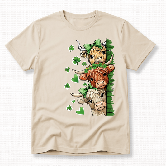 St. Patrick’s Day Highland Cow Graphic t-shirt featuring three cows with green bows and shamrocks on a sand t-shirt