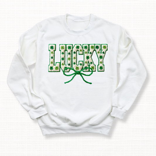 St. Patrick’s Day crewneck sweatshirt with textured “Lucky” lettering filled with green shamrocks and topped with a green ribbon bow on a white crewneck sweatshirt.