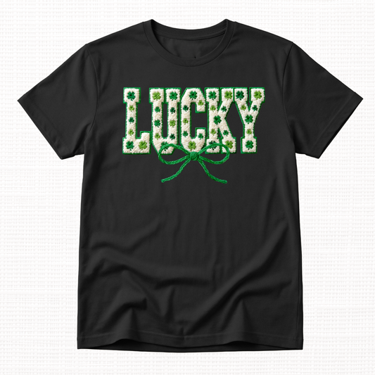 St. Patrick’s Day t-shirt featuring textured “Lucky” lettering filled with green shamrocks and topped with a green ribbon bow on a black t-shirt