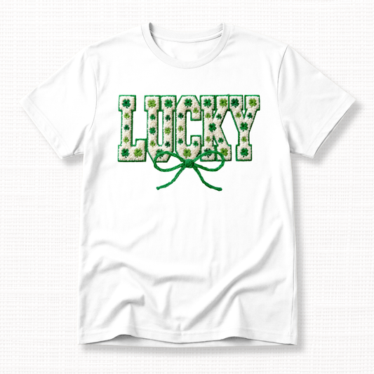 St. Patrick’s Day t-shirt featuring textured “Lucky” lettering filled with green shamrocks and topped with a green ribbon bow on a white t-shirt