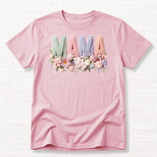 Light pink t-shirt with “MAMA” in pastel crochet-style lettering, framed at the bottom with a bouquet of soft floral accents.