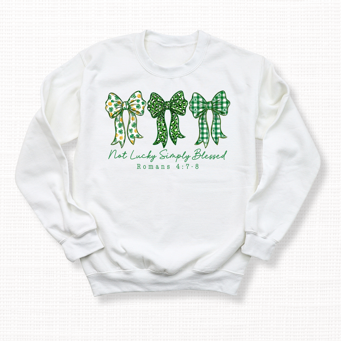 White crewneck sweatshirt with three green bows and the phrase “Not Lucky Simply Blessed” with Romans 4:7-8