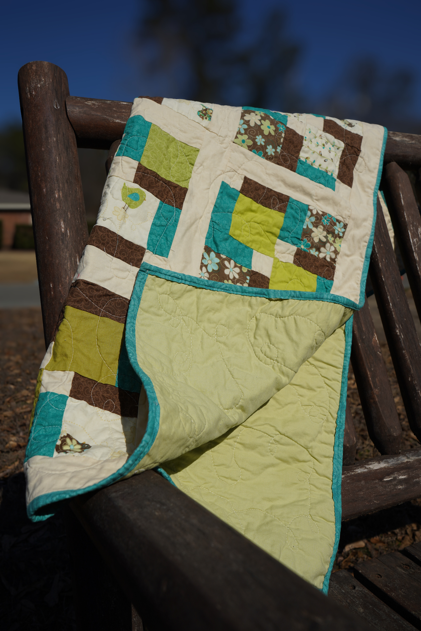 handmade disappearing nine patch baby quilt brown green aqua patchwork 35x44 draped over a wooden bench showing the light green backing.