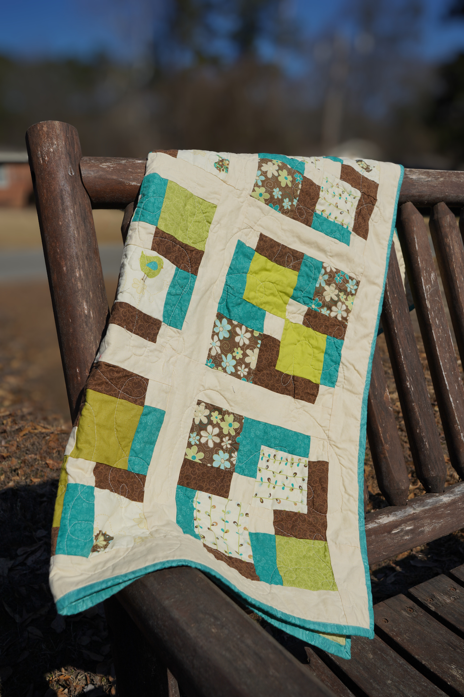 handmade disappearing nine patch baby quilt brown green aqua patchwork 35x44 draped over a wooden bench