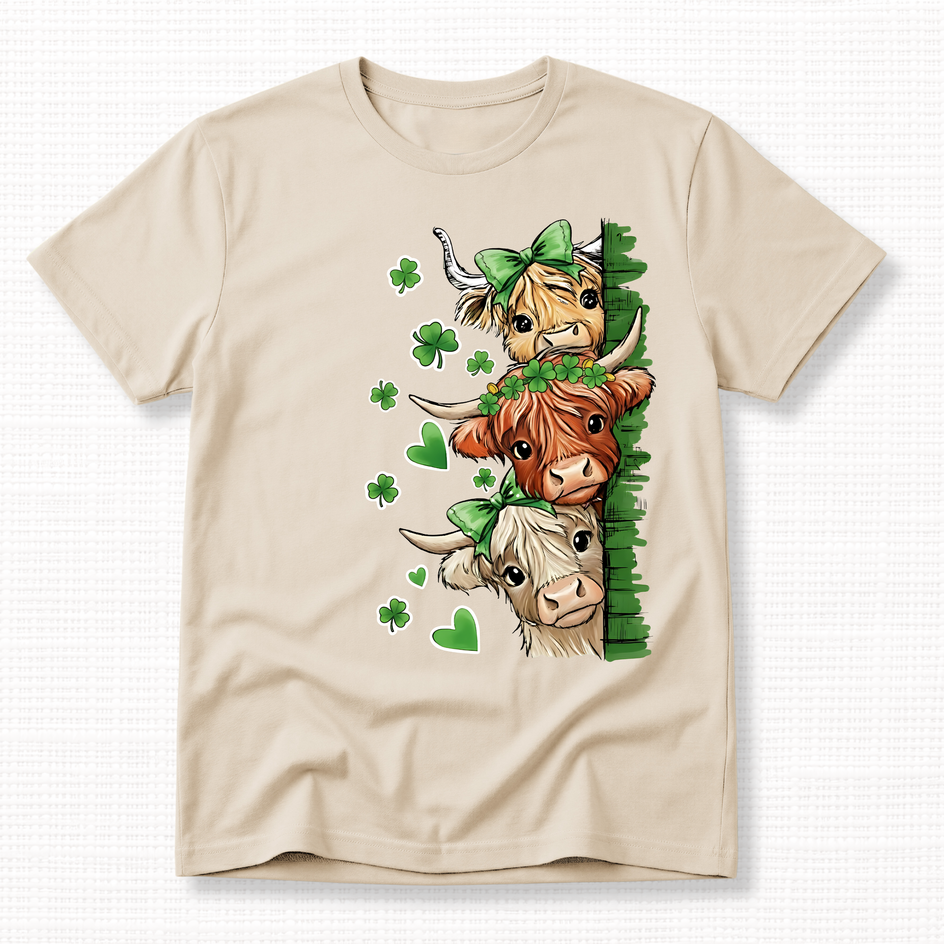 St. Patrick’s Day Highland Cow Graphic t-shirt featuring three cows with green bows and shamrocks on a sand t-shirt