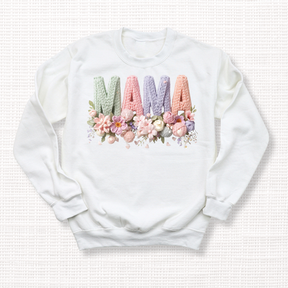 White crewneck sweatshirt with “MAMA” in pastel crochet-style lettering, framed at the bottom with a bouquet of soft floral accents.
