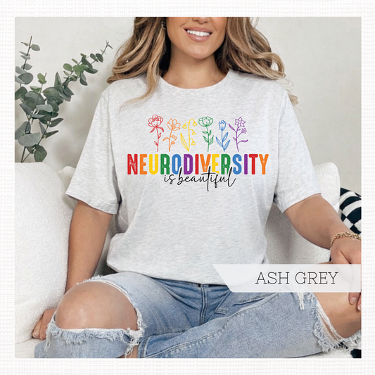 Person wearing an ash grey t-shirt with rainbow 'Neurodiversity is beautiful' text and colorful flowers.